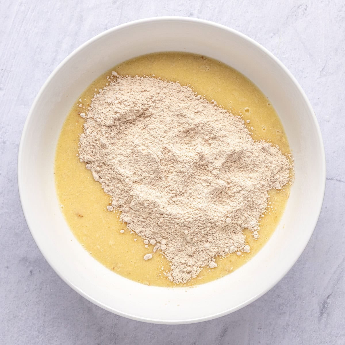 Wet ingredients for muffin batter in a bowl with dry ingredients on top before combining.