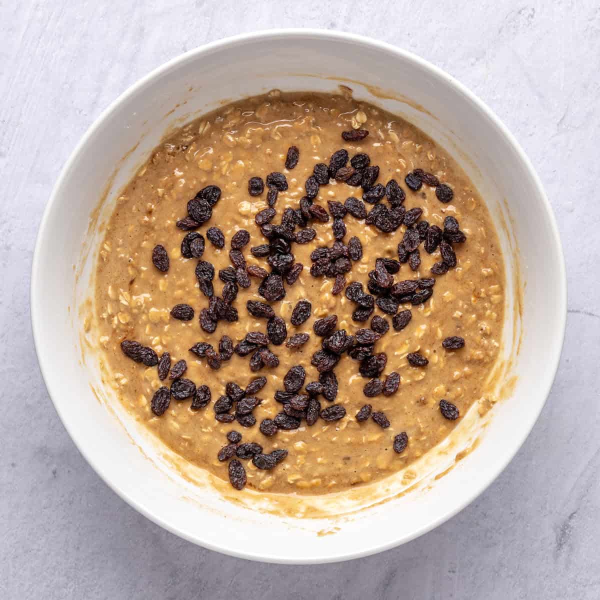 Oatmeal muffin batter in a bowl with raisins added before folding in.