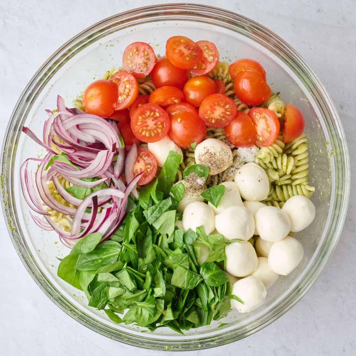 Mozzarella, tomatoes, spinach, onion, salt and pepper added to pesto pasta before tossing.