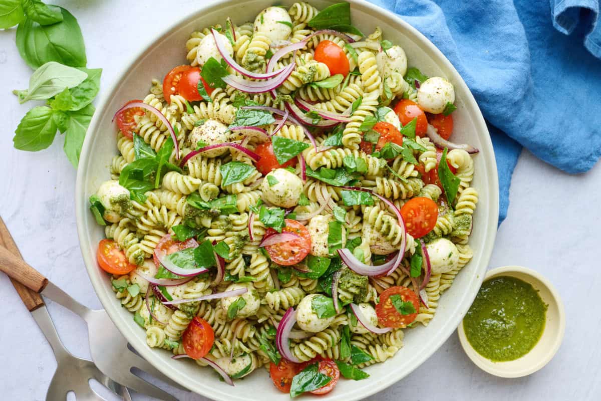 Easy pesto pasta salad with tomato, mozzarella balls, and spinach in a serving bowl.