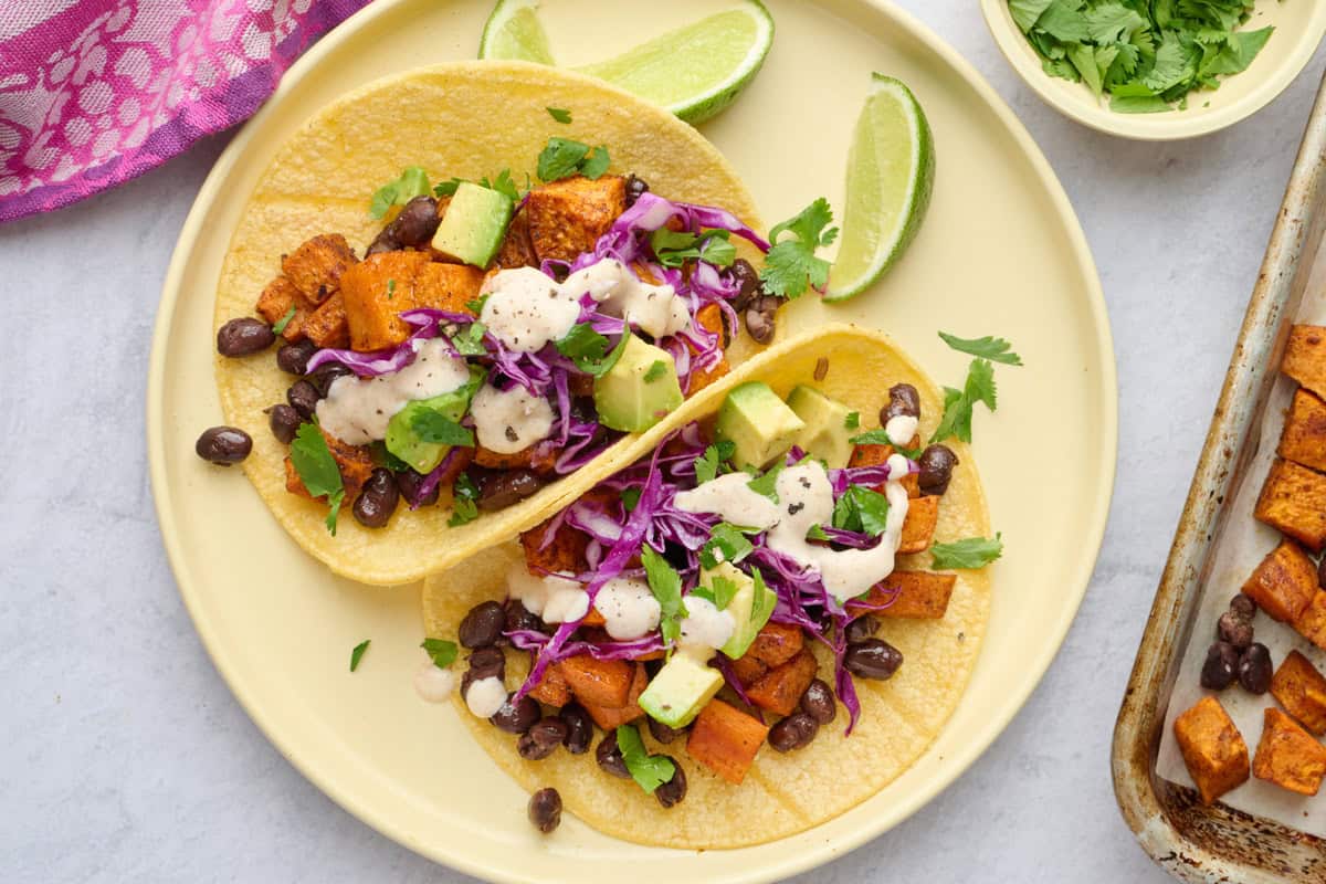 Hearty sweet potato tacos on a small plate with sauce lightly drizzled on top.