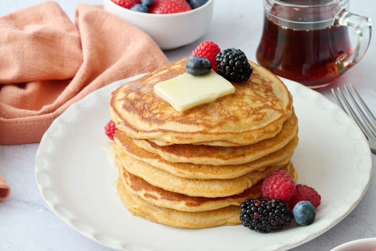Best whole wheat pancakes on a plate topped with butter and fresh fruit.