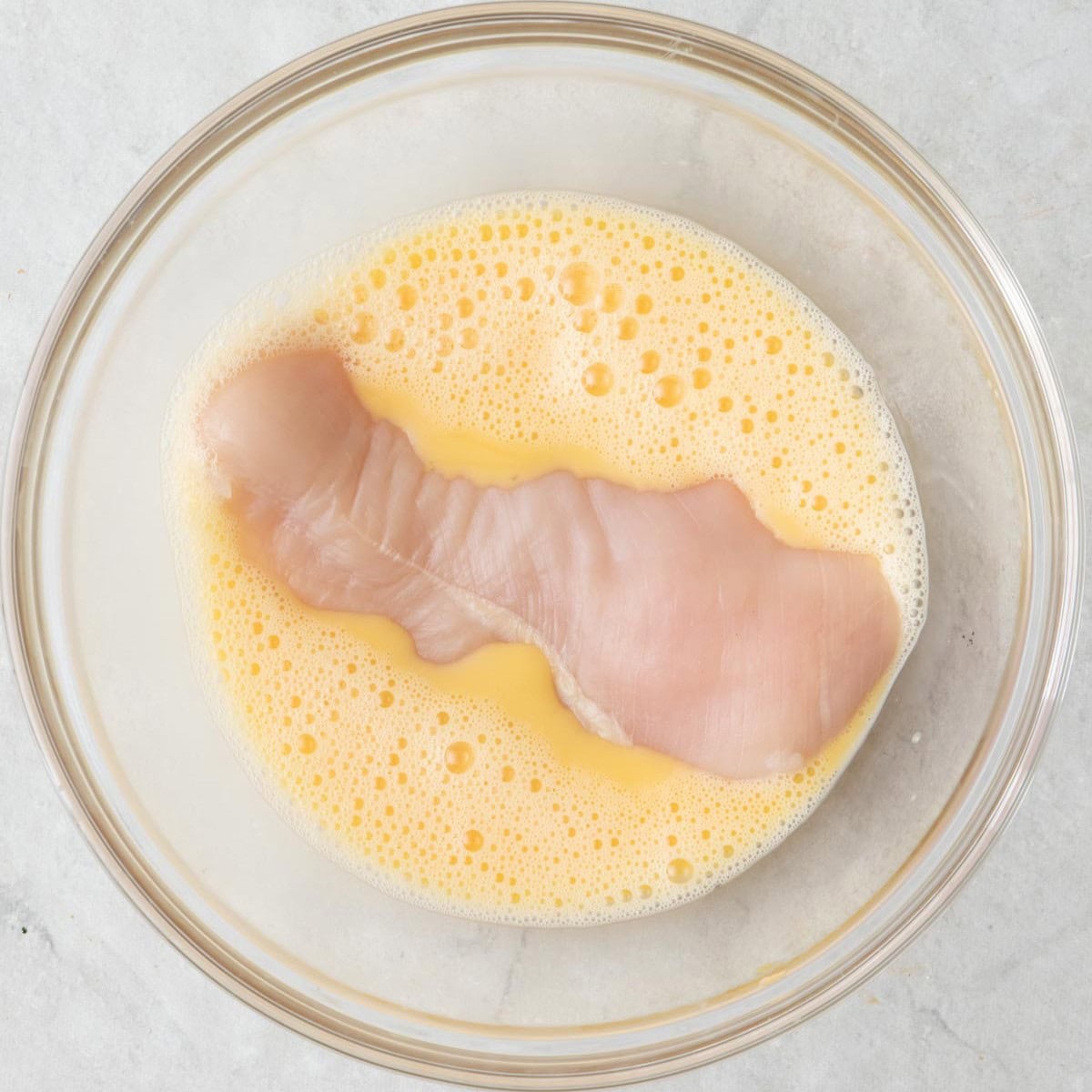 Chicken cutlet's in a bowl of whisked eggs before coating with almond mixture.