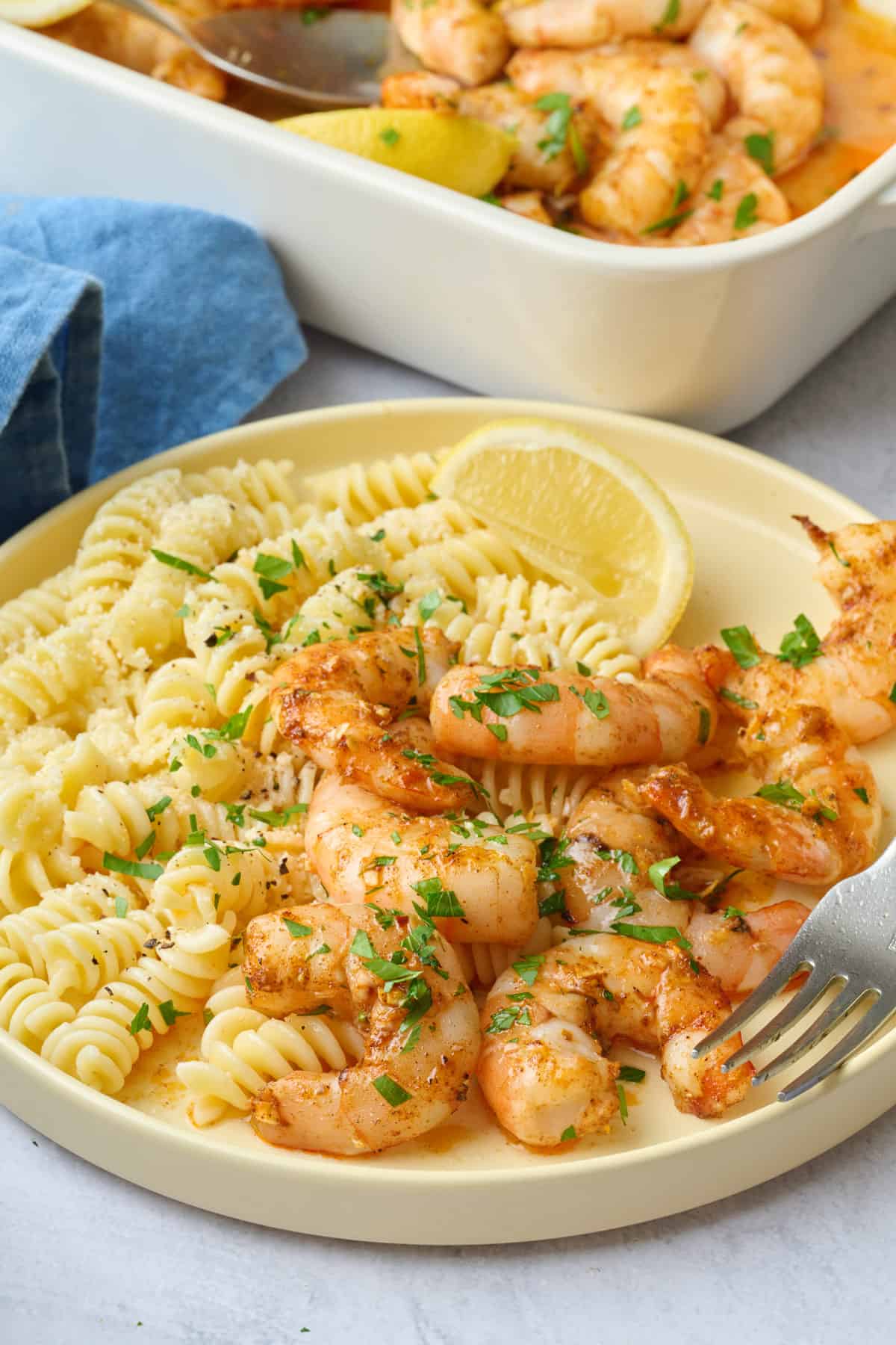 Best baked shrimp served with pasta and lemon wedges with baking dish nearby.