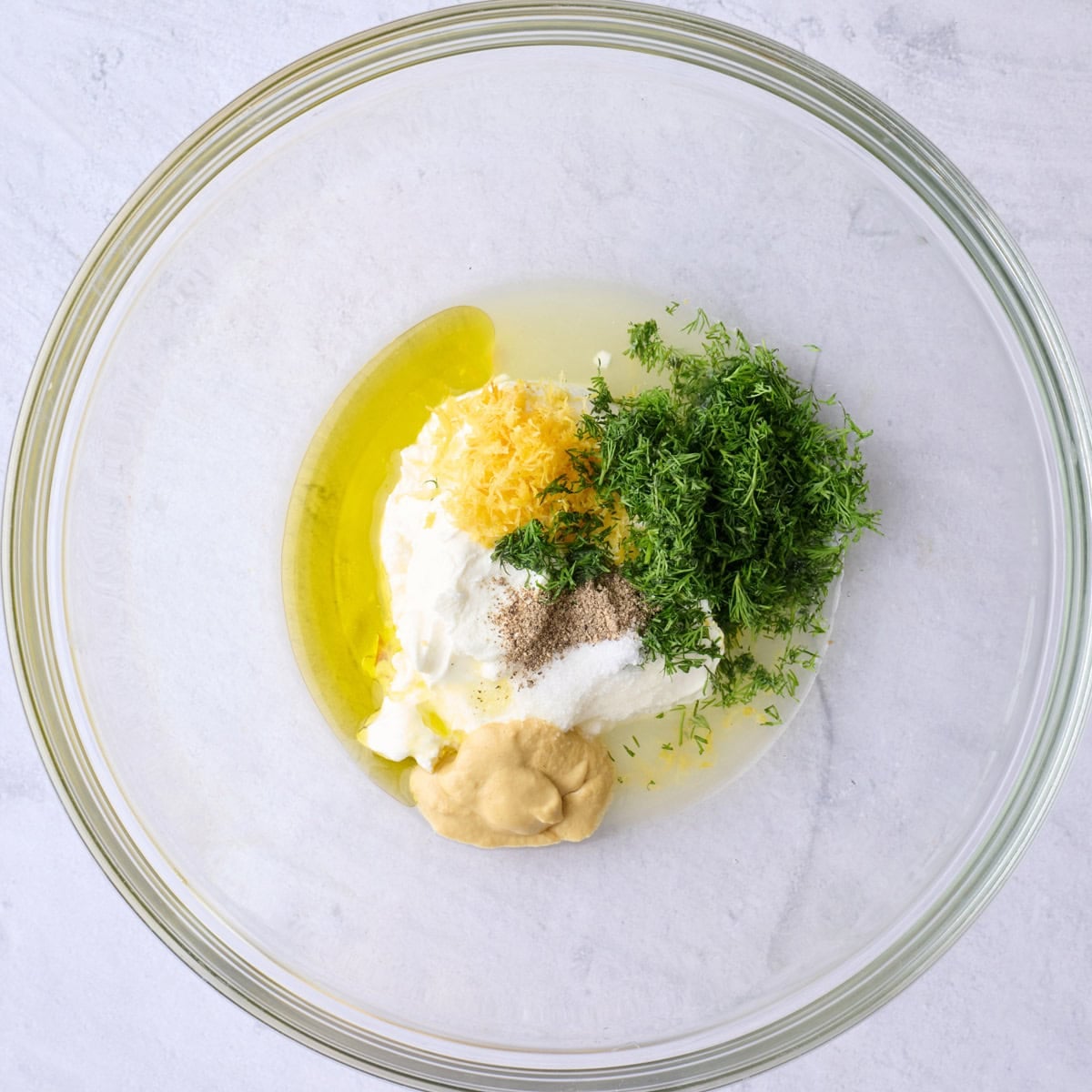 Yogurt, olive oil, lemon zest and juice, dill, mustard, salt and pepper in a large bowl before mixing.