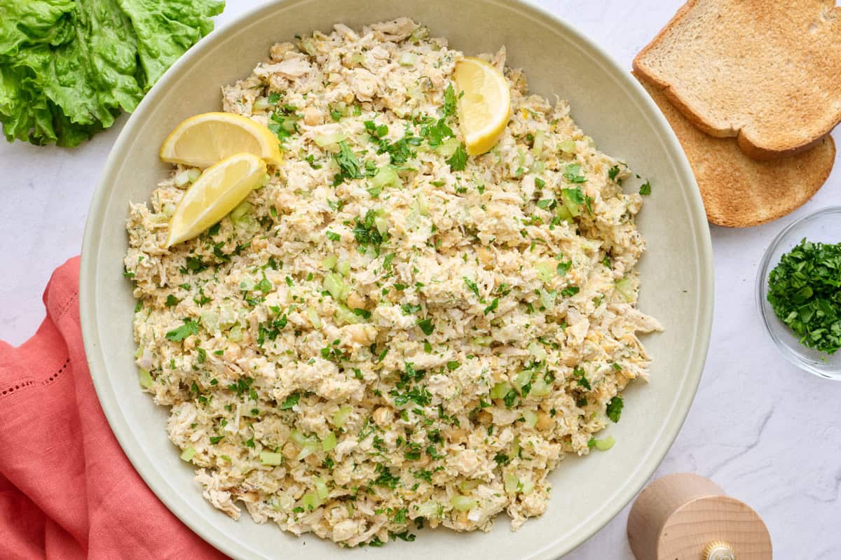 Best chicken chickpea chicken salad in a serving bowl garnished with lemon wedges and served with toast and lettuce.