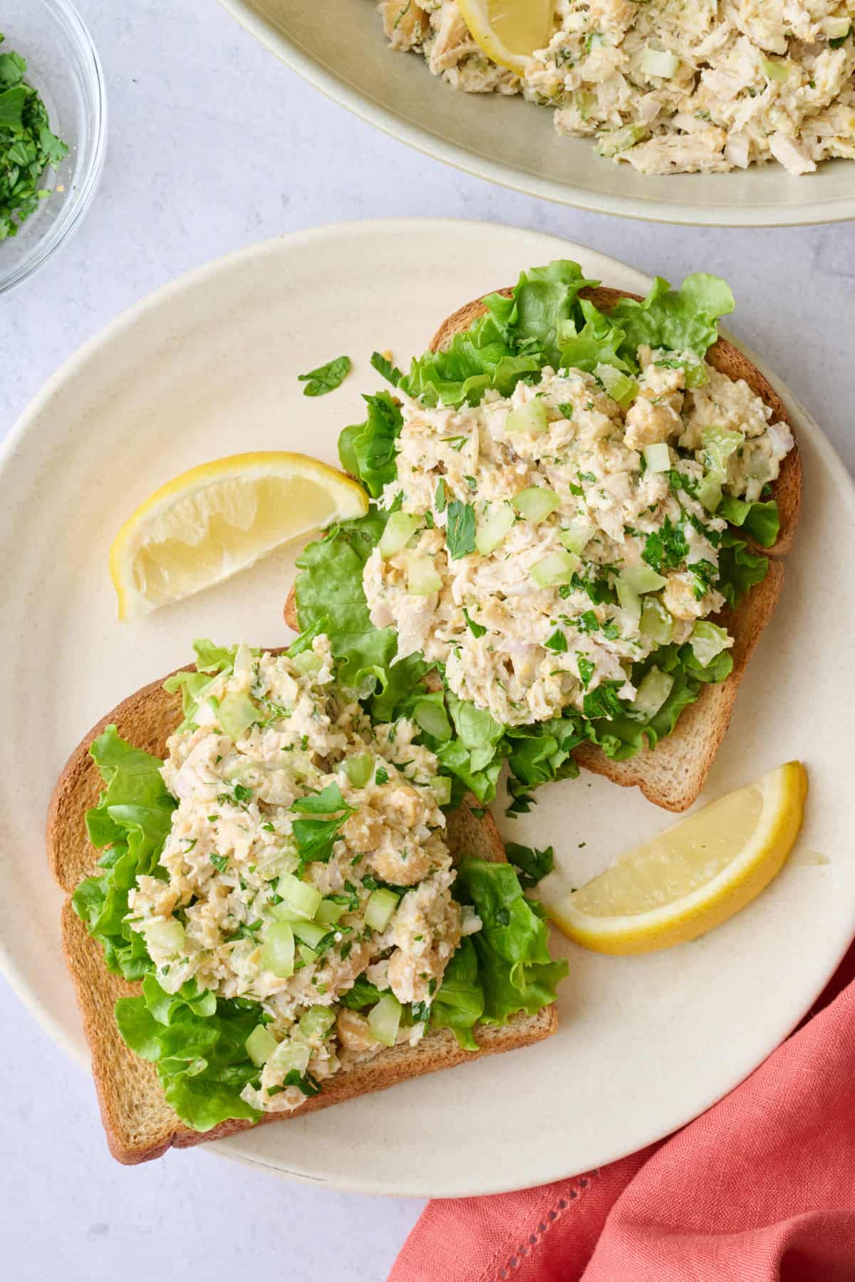 Simple chicken chickpea salad served over toast and lettuce with serving bowl nearby.