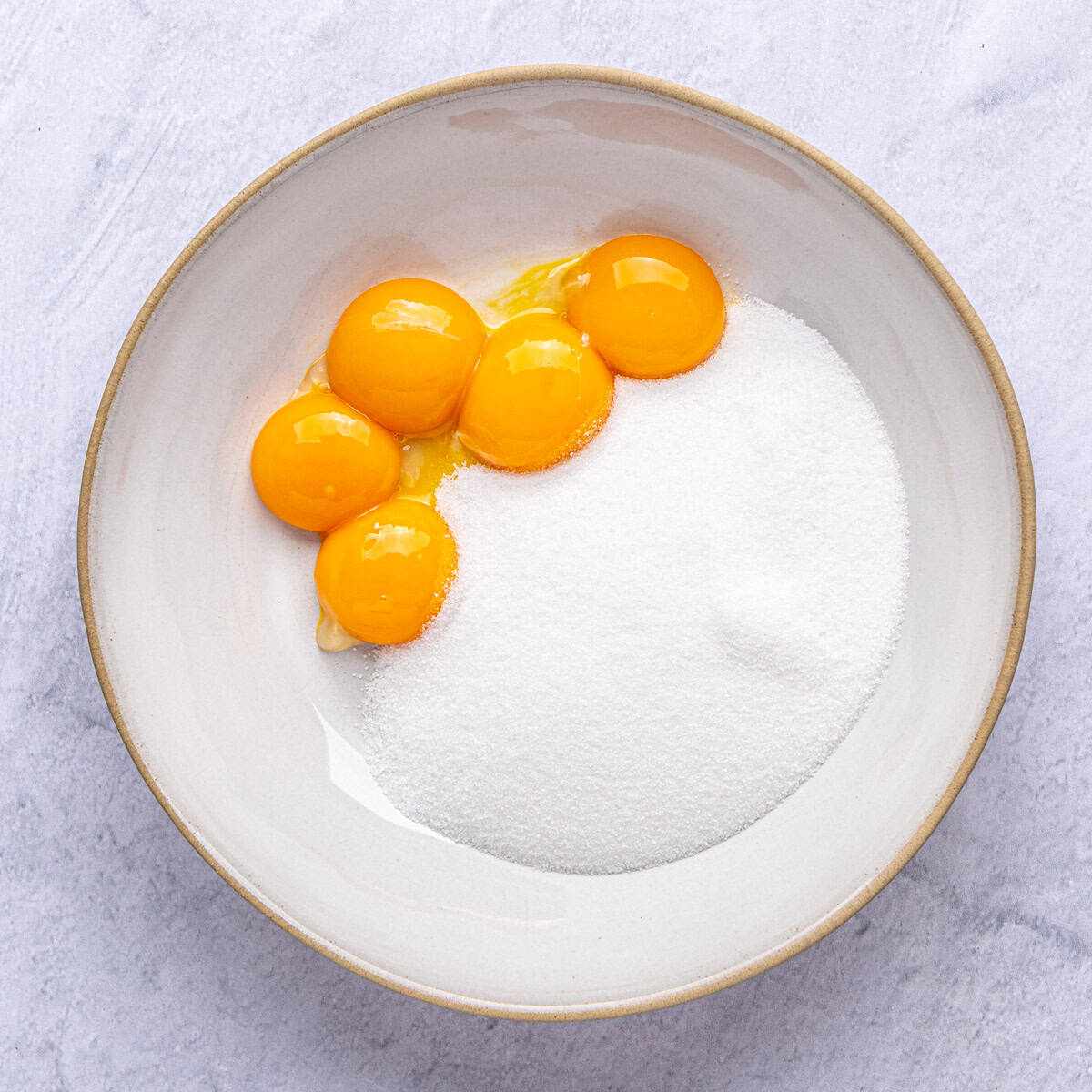 Sugar and egg yolks in a bowl before mixing together for custard.