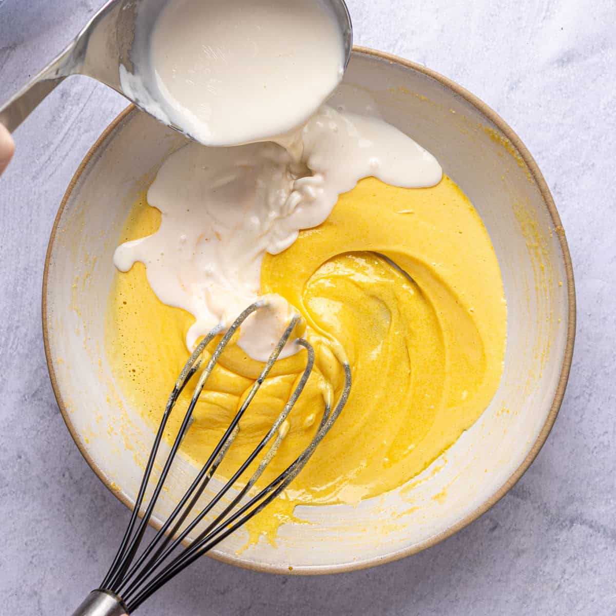 Egg and sugar mixture after combining with warmed milk being whisked in.