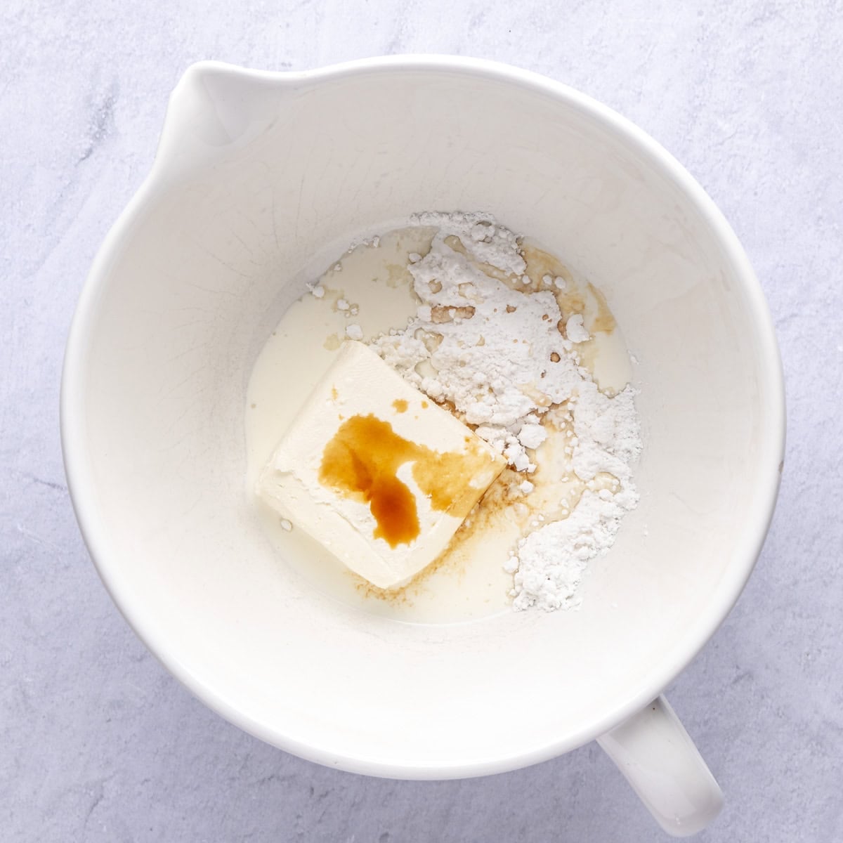 Cream cheese, powdered sugar, vanilla, and heavy cream in a bowl before mixing for no bake cheesecake filling.