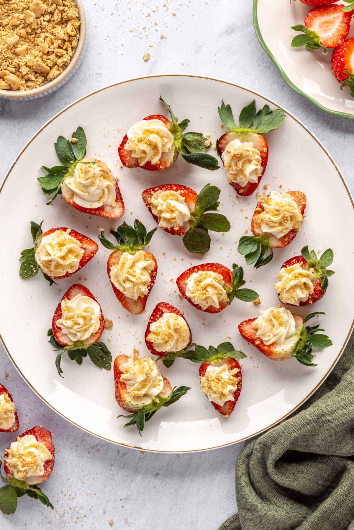 No-bake cheesecake deviled strawberries on a platter with extra crushed graham crackers nearby.