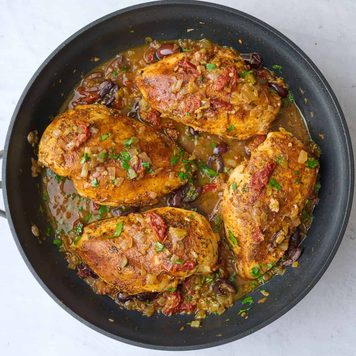 Chicken breast recipe after parsley is stirred into Mediterranean sauce in skillet.