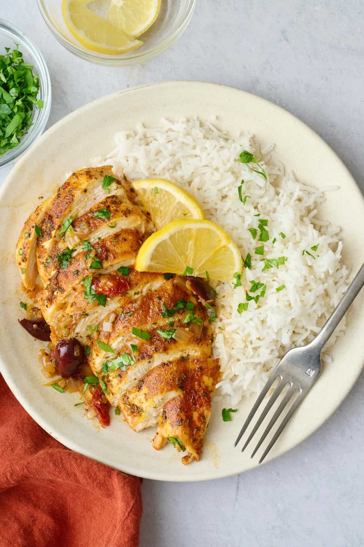 Sliced chicken breast with sun dried tomato and olive sauce on a plate with rice and lemon.