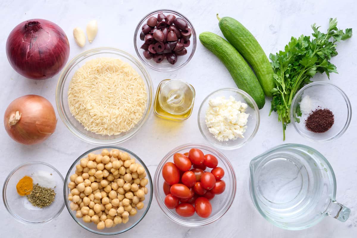 Ingredients for Mediterranean bowl recipe: rice, red onion, yellow onion, salt, oregano, turmeric, garlic, chickpeas, olives, oil, tomatoes, feta, cucumbers, parsley, salt, sumac, and water.