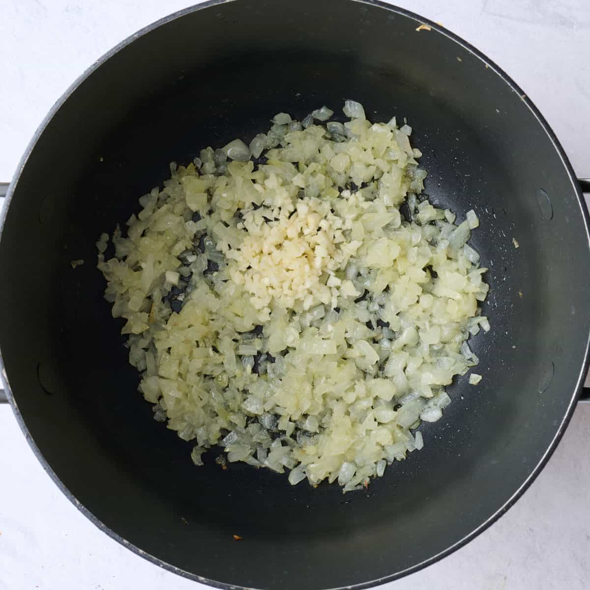 Cooked onions in saucepan with garlic added before stirring.
