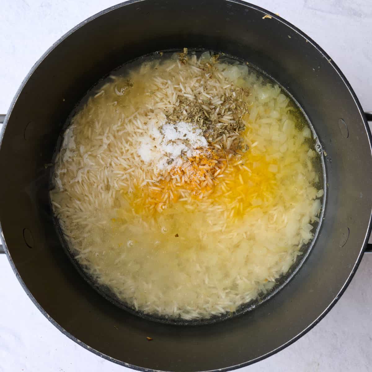 Rice, water, salt, oregano, and turmeric added to pan with onions and garlic before combining.
