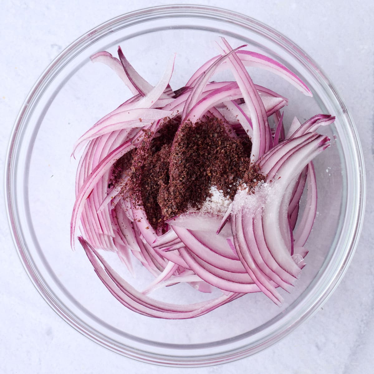 Sliced red onions, sumac and salt in a small bowl before combining.