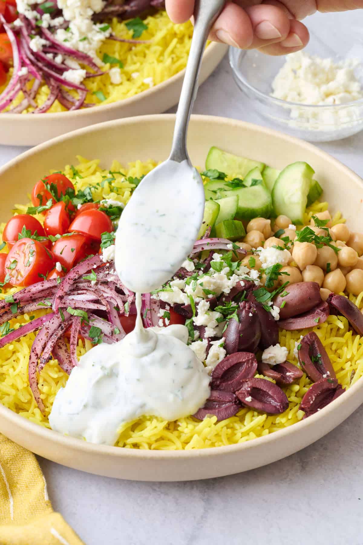 Best rice bowl recipe with Mediterranean toppings and a greek yogurt sauce being drizzled on top.