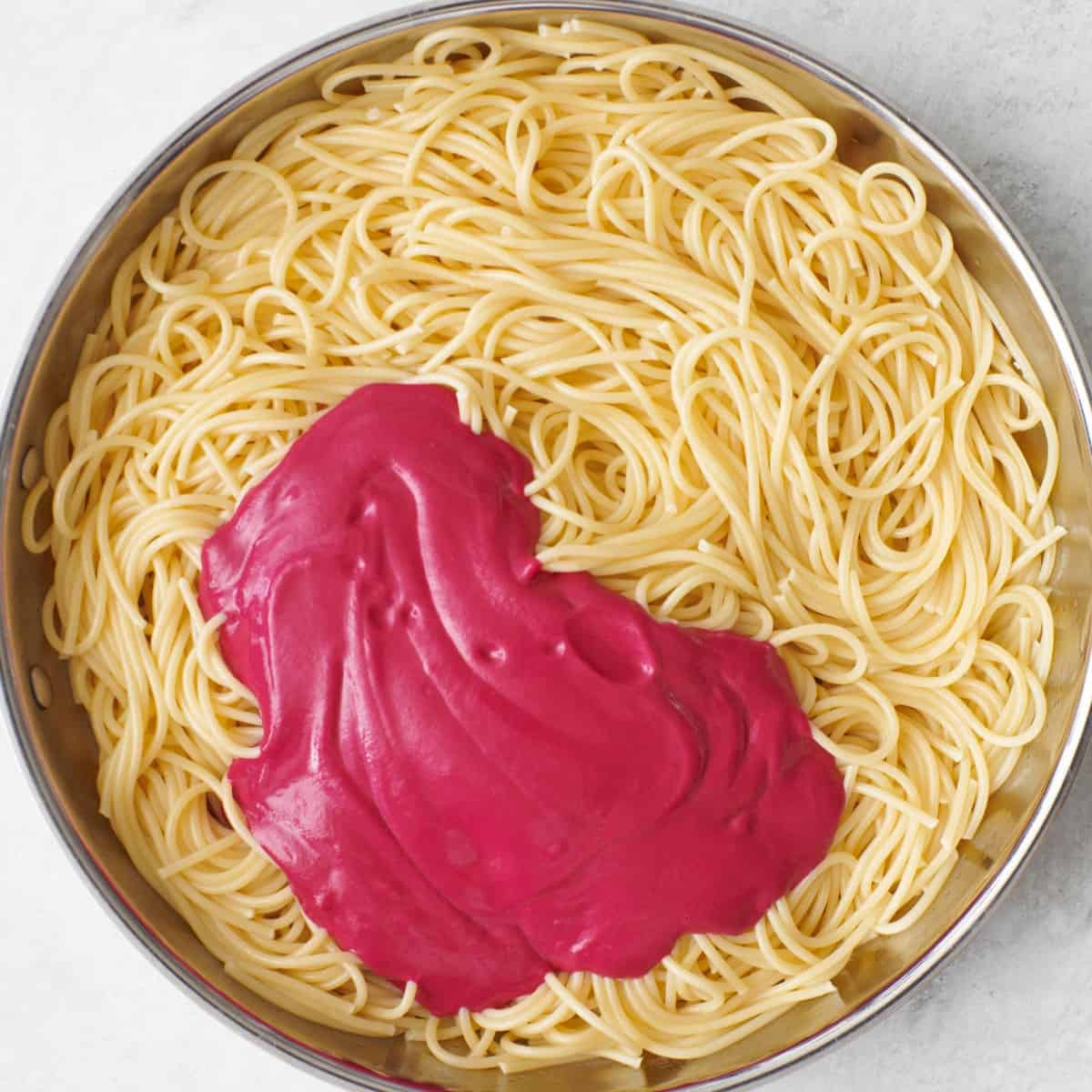 Creamy pink roasted beet sauce added on top of pasta in pan.
