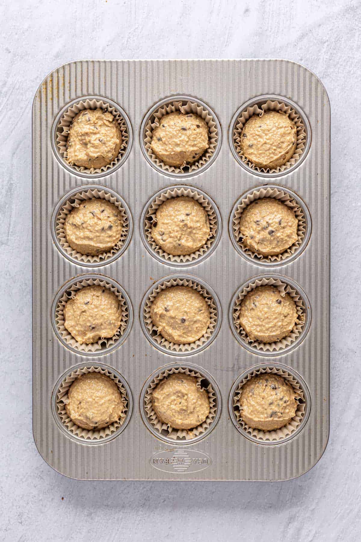 Protein muffin batter made with cottage cheese and vanilla protein powder divided into a 12 cup muffin pan before baking.
