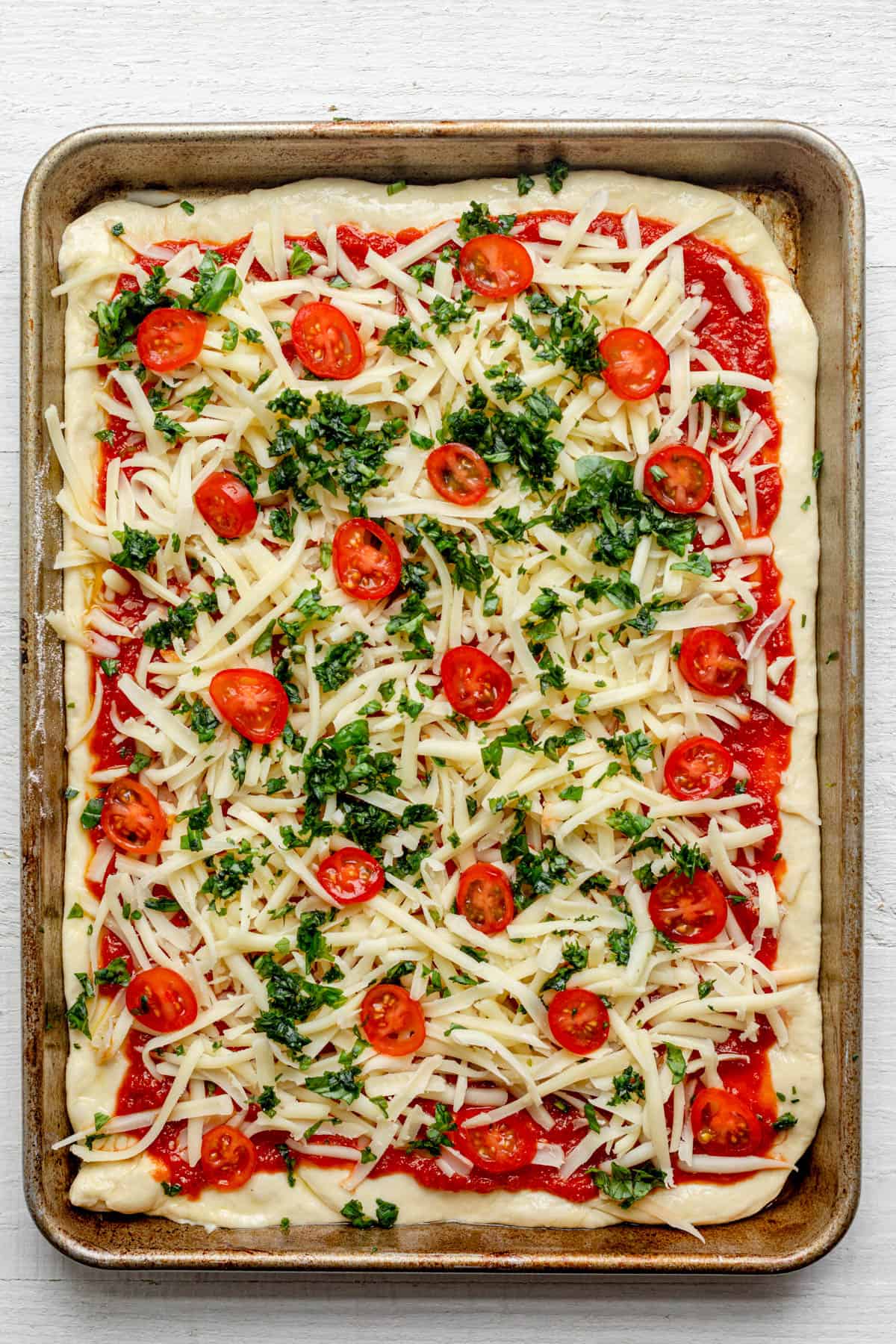 Uncooked pizza on a sheet pan with sauce, cheese and toppings added before baking.
