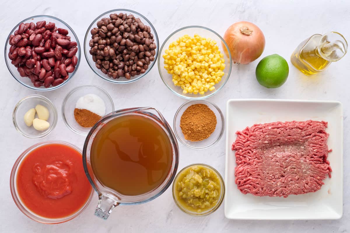 Ingredients for soup recipe: kidney beans, black beans, garlic, salt and taco seasoning, tomato sauce, broth, corn, chili powder, green chilis, onion, lime, oil, and ground beef.