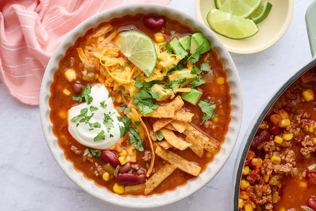 Bowl of beef and bean taco soup served in a bowl garnished with cheese, sour cream, avocado, tortilla strips, and cilantro.