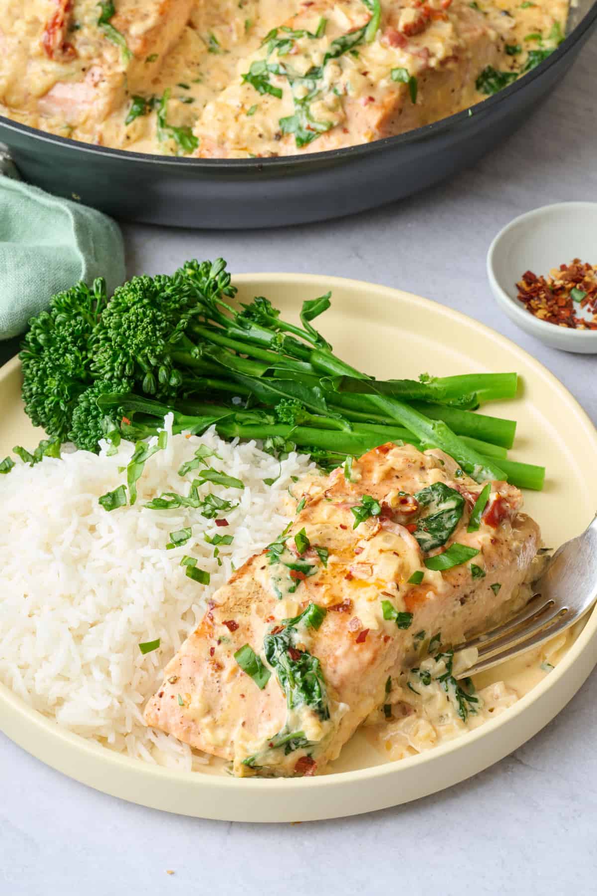 Serving of Tuscan salmon served on a plate with extra cream sauce, a side of rice, and broccoli.