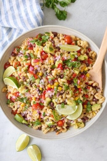 Bean and macaroni pasta salad recipe in a serving bowl garnished with cilantro and lime wedges.