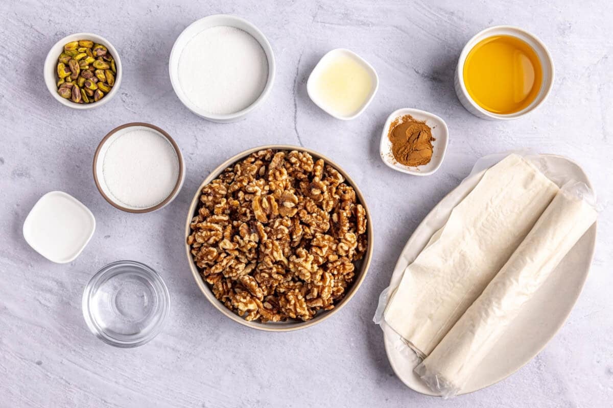Ingredients for baklava rolls recipe: phyllo sheets, walnuts, sugar, water, lemon juice, orange blossom water, cinnamon, ghee, and crushed pistachios.