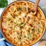 Chicken Parmesan Pasta in a pot with a wooden spoon, with ingredients for the recipe surrounding.