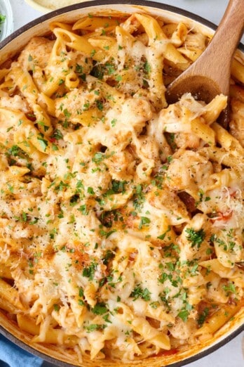 Chicken Parmesan Pasta in a pot with a wooden spoon, with ingredients for the recipe surrounding.