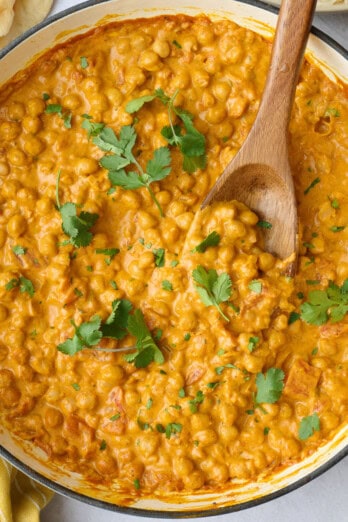 Chickpea curry in the skillet garnished with cilantro, with a dish of basmati rice and naan nearby.