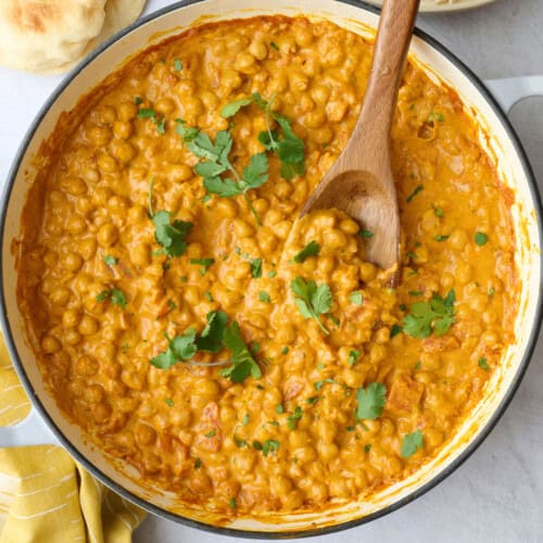 Chickpea curry in the skillet garnished with cilantro, with a dish of basmati rice and naan nearby.
