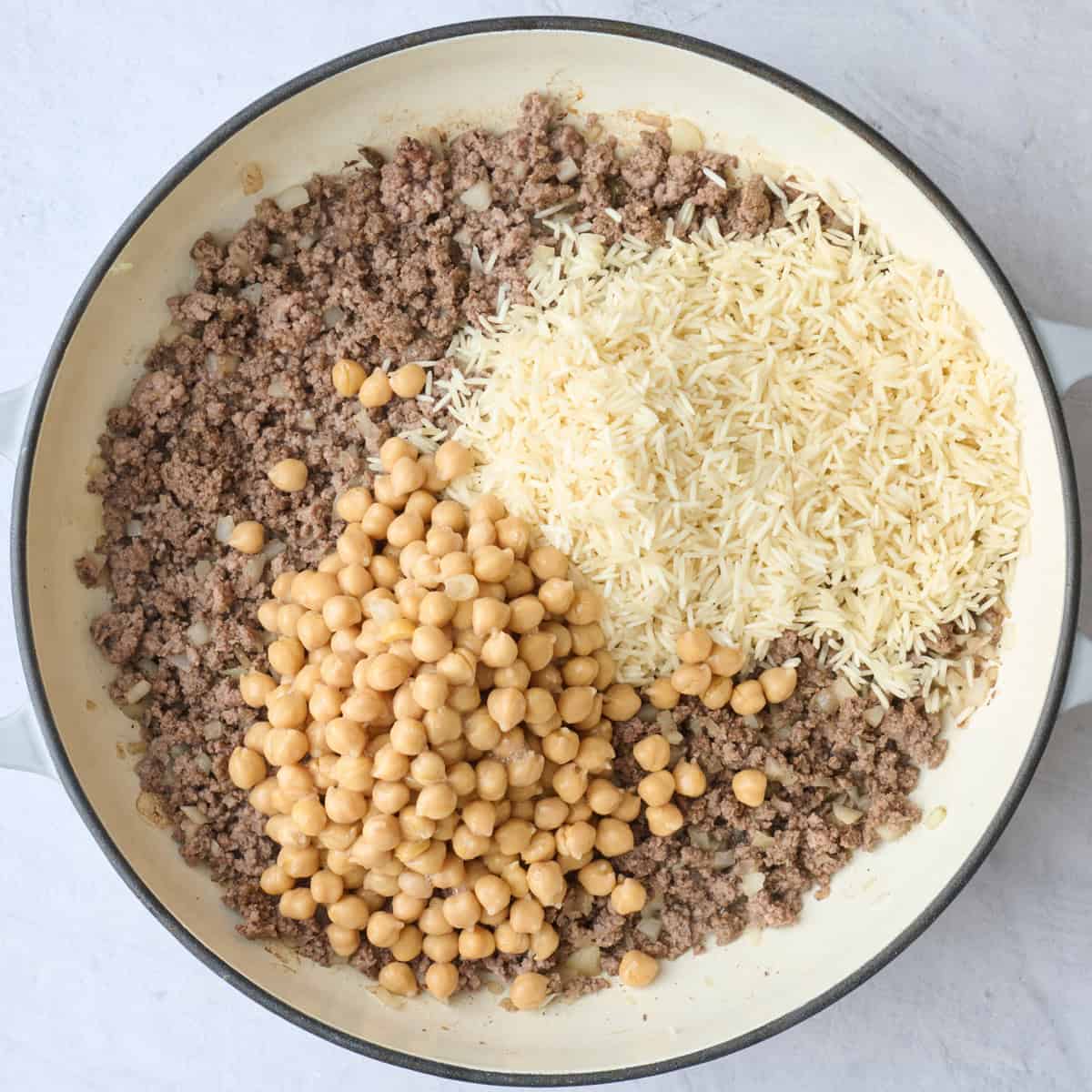 Rinsed rice and chickpeas added to pot with spiced ground beef and onions before combining.