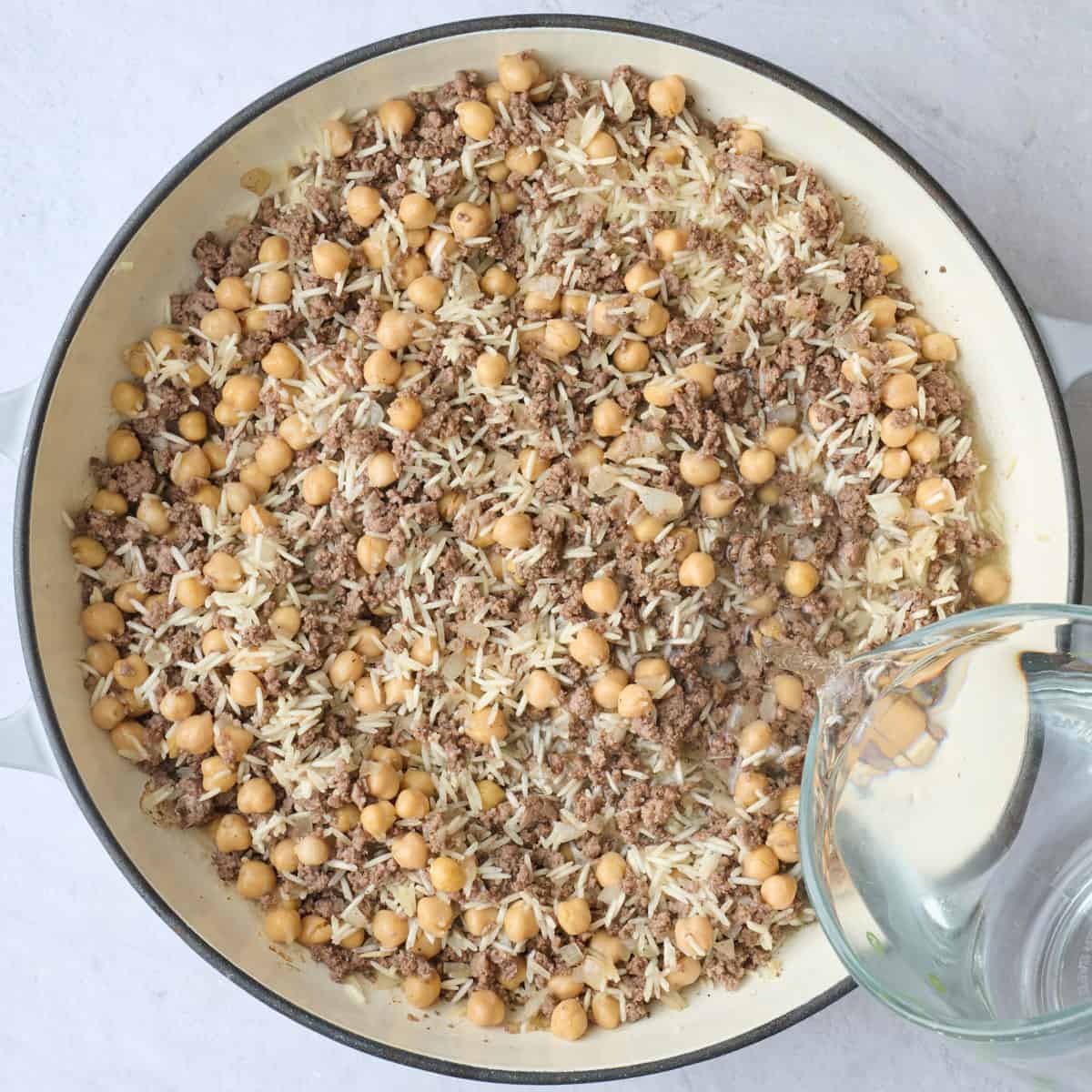 Water being added to cooked ground beef with uncooked rice and chickpeas.