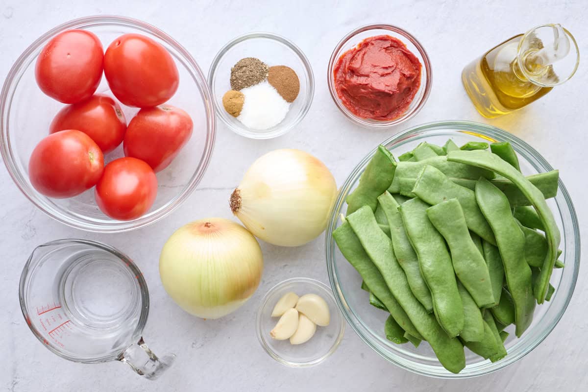 Ingredients for Lebanese side dish recipe: tomatoes, water, spices, onions, garlic, tomato paste, oil, garlic, and flat Italian green beans.