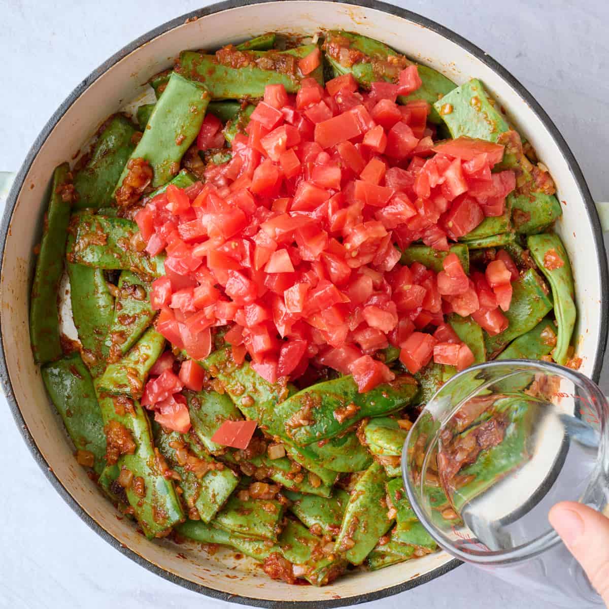 Chopped tomato and water added to spiced green beans before cooking.
