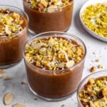 Three dessert bowls of meghli, staggered with extra ingredients around.