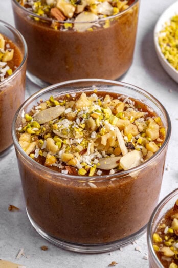 Three dessert bowls of meghli, staggered with extra ingredients around.