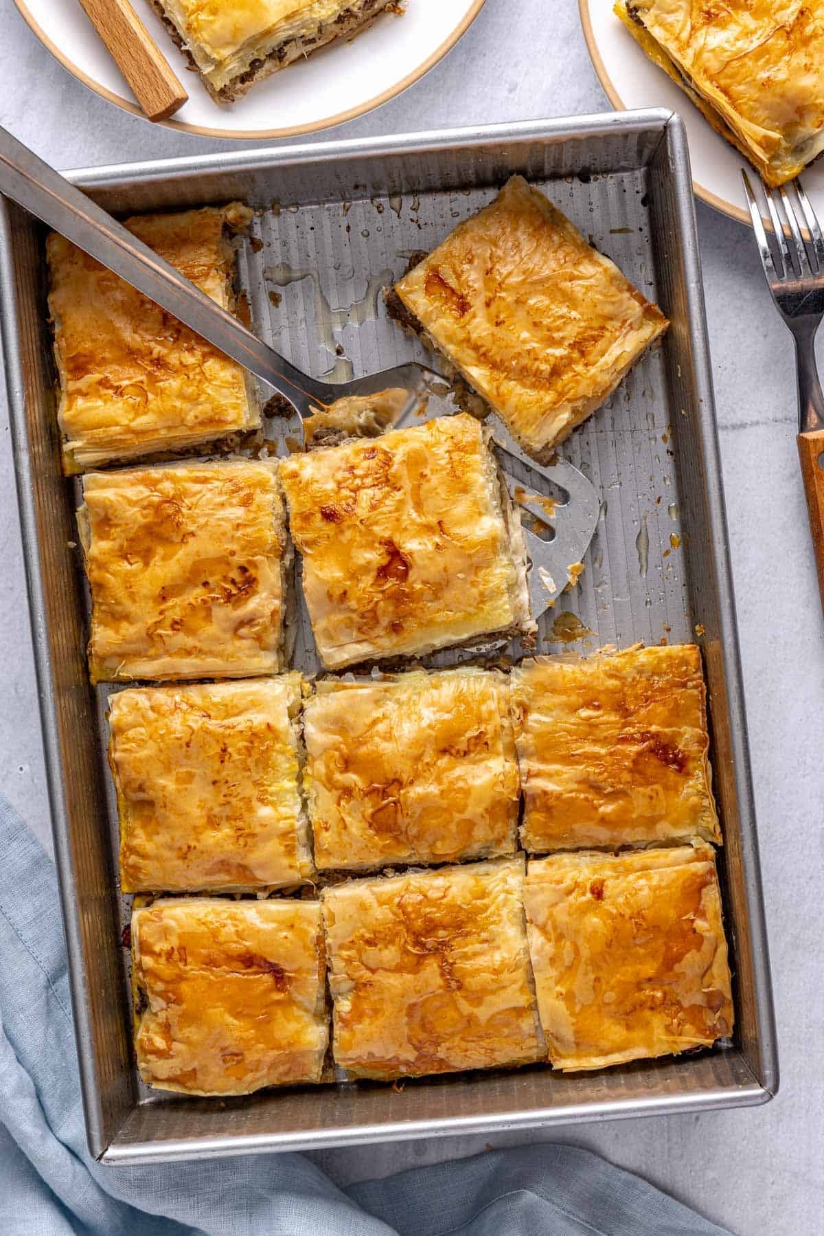 Meat pie in baking dish with 2-3 pieces removed to a small serving plate nearby, spatula resting in pan.