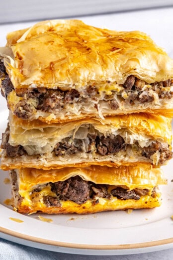 2-3 meat pie squares stacked on a small plate with baking dish in background.
