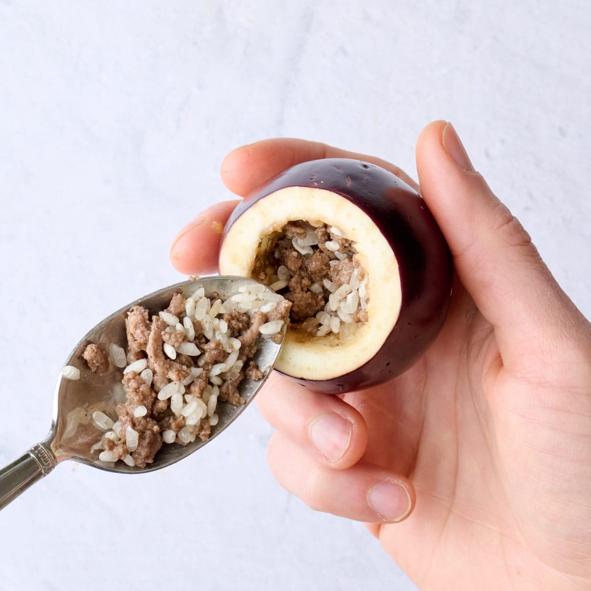 Beef and rice mixture being spooned into a hollowed out baby eggplant.