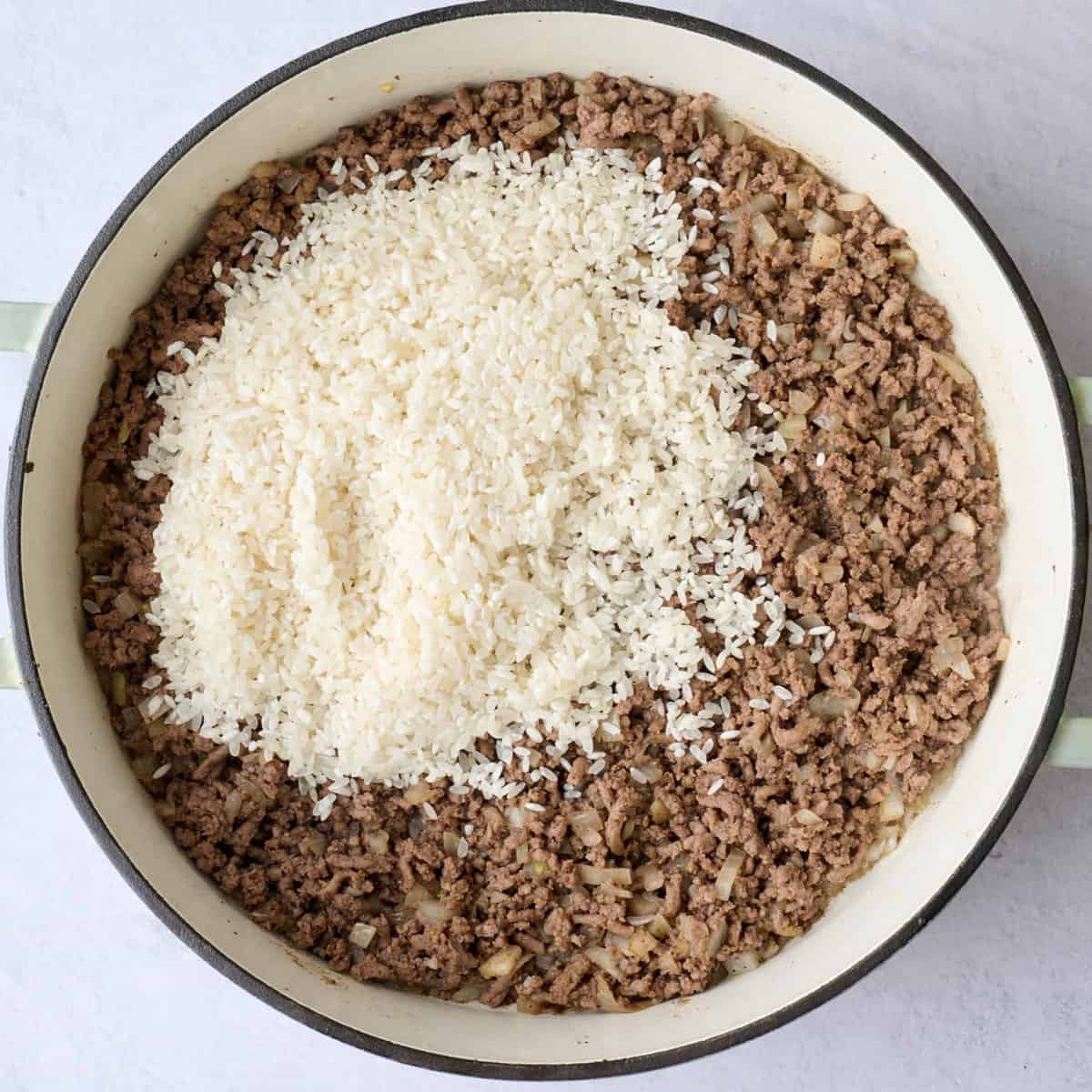 Rice added to cooked ground beef in a pot.