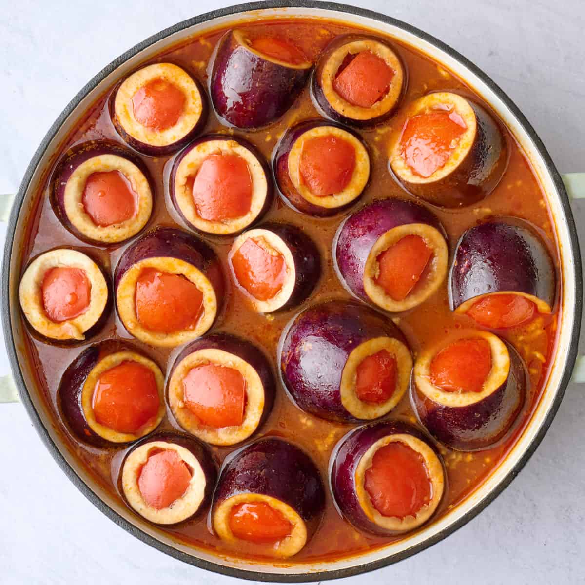 Stuffed baby eggplants added to tomato broth before cooking.