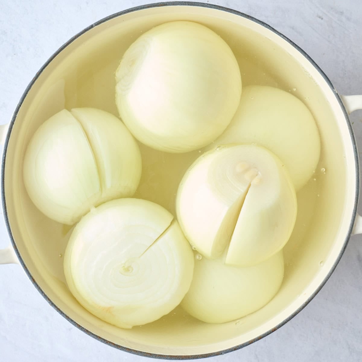 Prepped whole onions with a cut made to the core in a pot of water before softening for recipe.