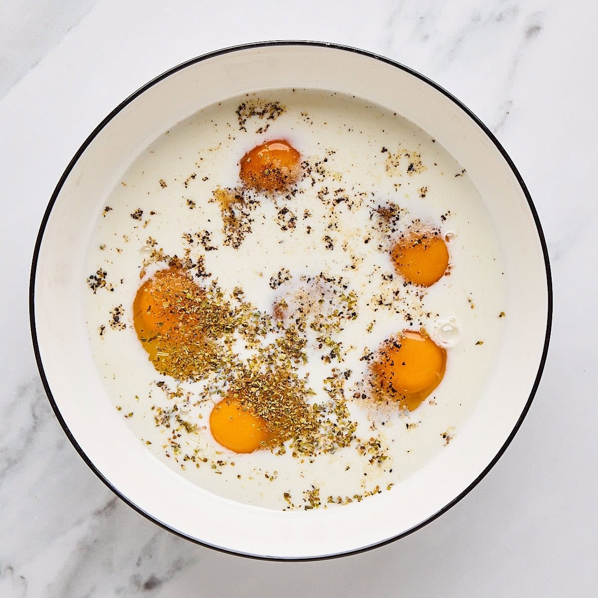 Eggs, milk, garlic powder, oregano, salt and pepper in a bowl.