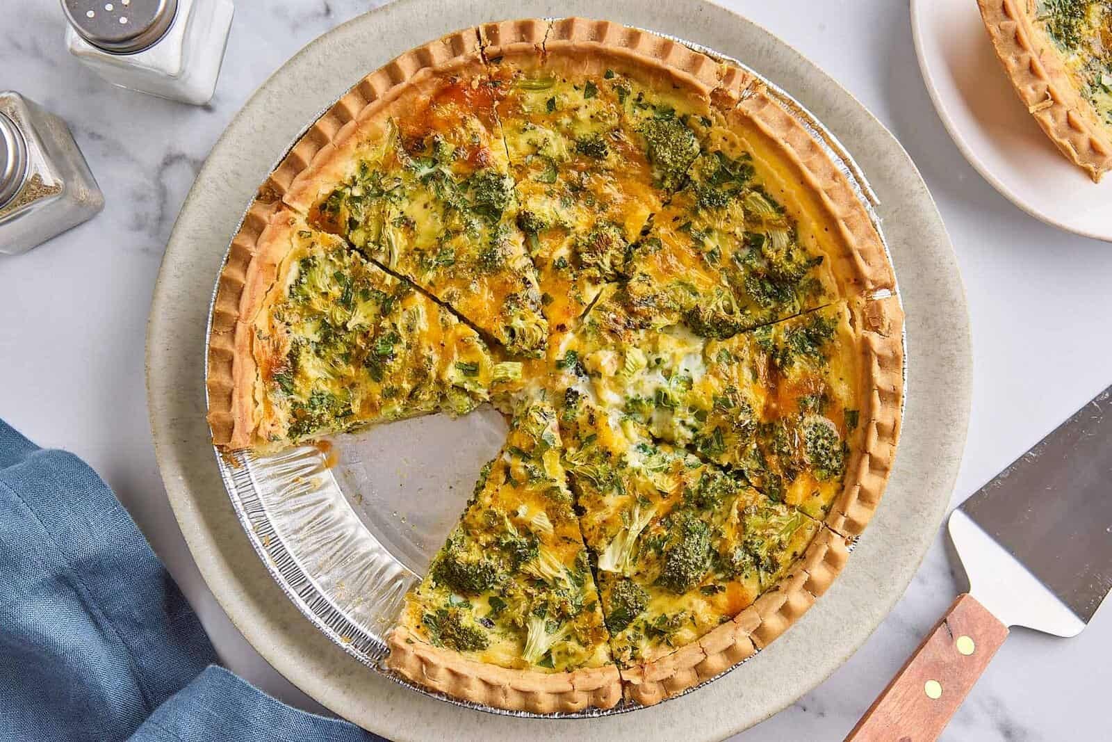Broccoli cheese quiche cut into 8 slices, one slice removed to plate nearby.