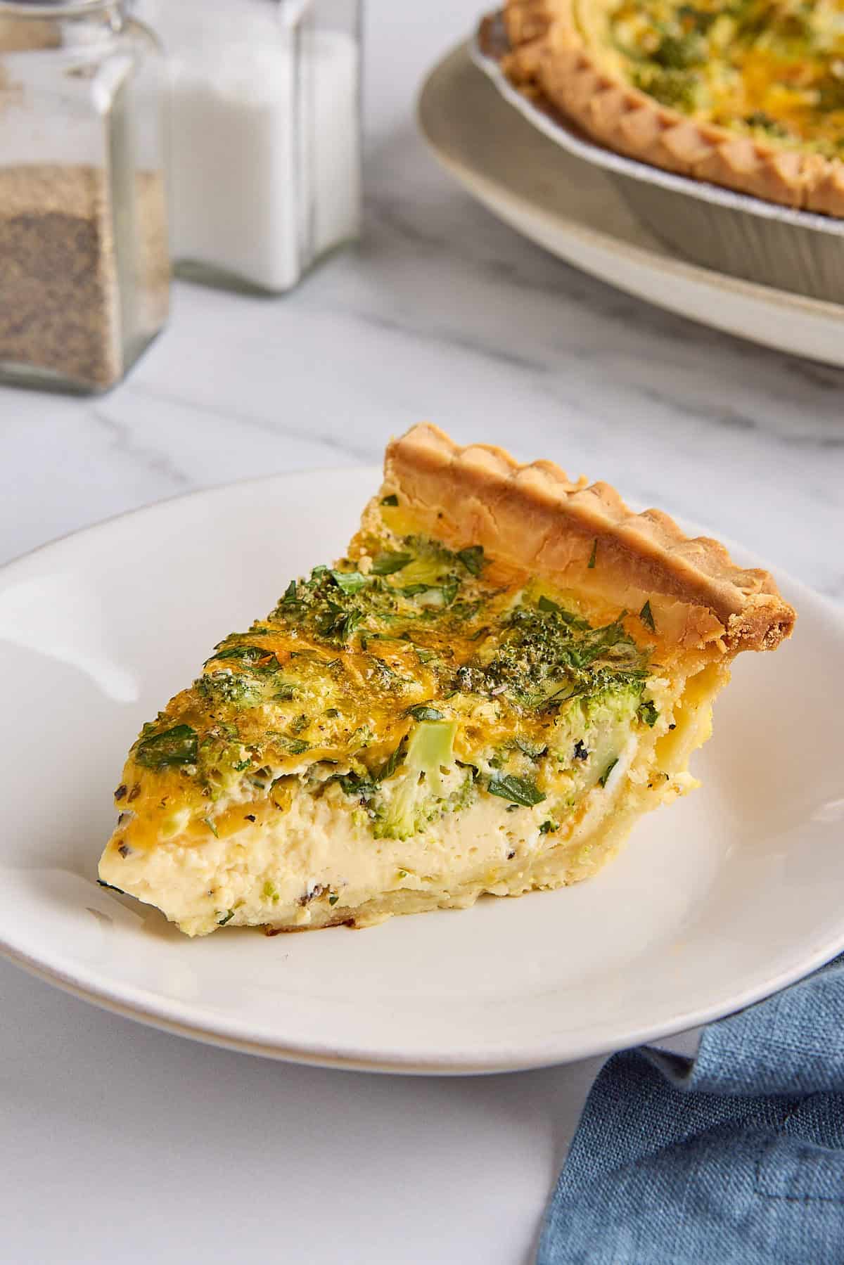 Easy broccoli and cheddar cheese quiche slice on a plate while whole quiche nearby.
