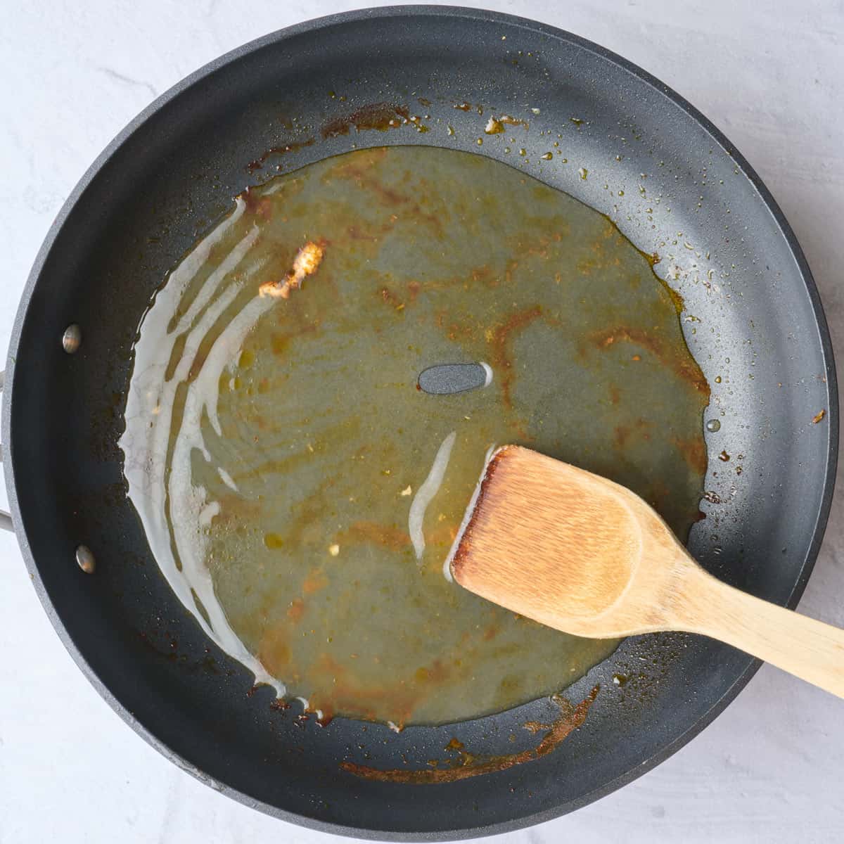 Chicken removed from skillet with broth added and spoon scraping bottom of pan.